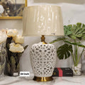 reticulated white ceramic table lamp with a brass base and a tapered fabric drum shade.